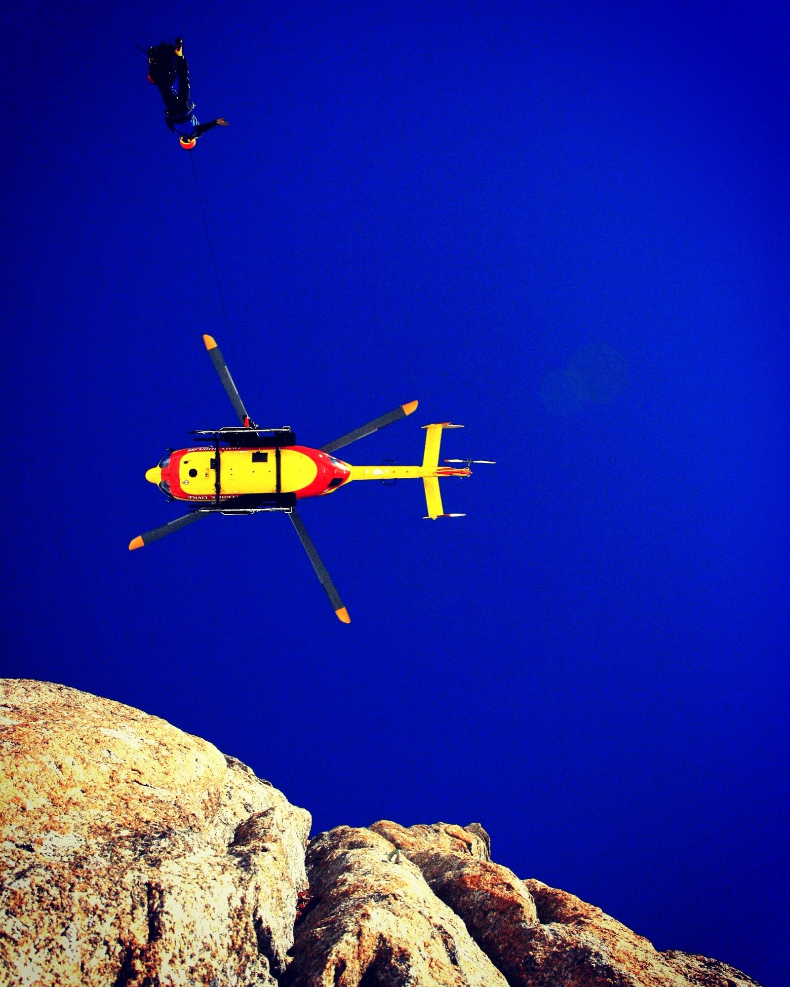 Un secouriste suspendu au câble de treuil d'un hélicoptère de la Sécurité civile, au-dessus d'une arête rocheuse