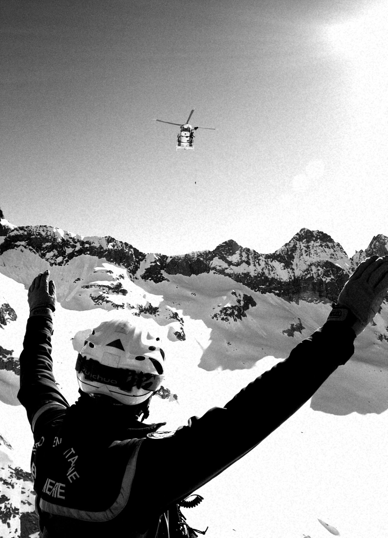 Un secouriste guide l'hélicoptère à l'atterrissage, bras levés, en haute montagne enneigée